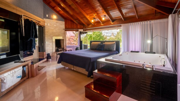 A modern bedroom with a large bed, a built-in TV, a bathtub, and a view of the outdoors. - FIKA Residence (Dois Irmaos)