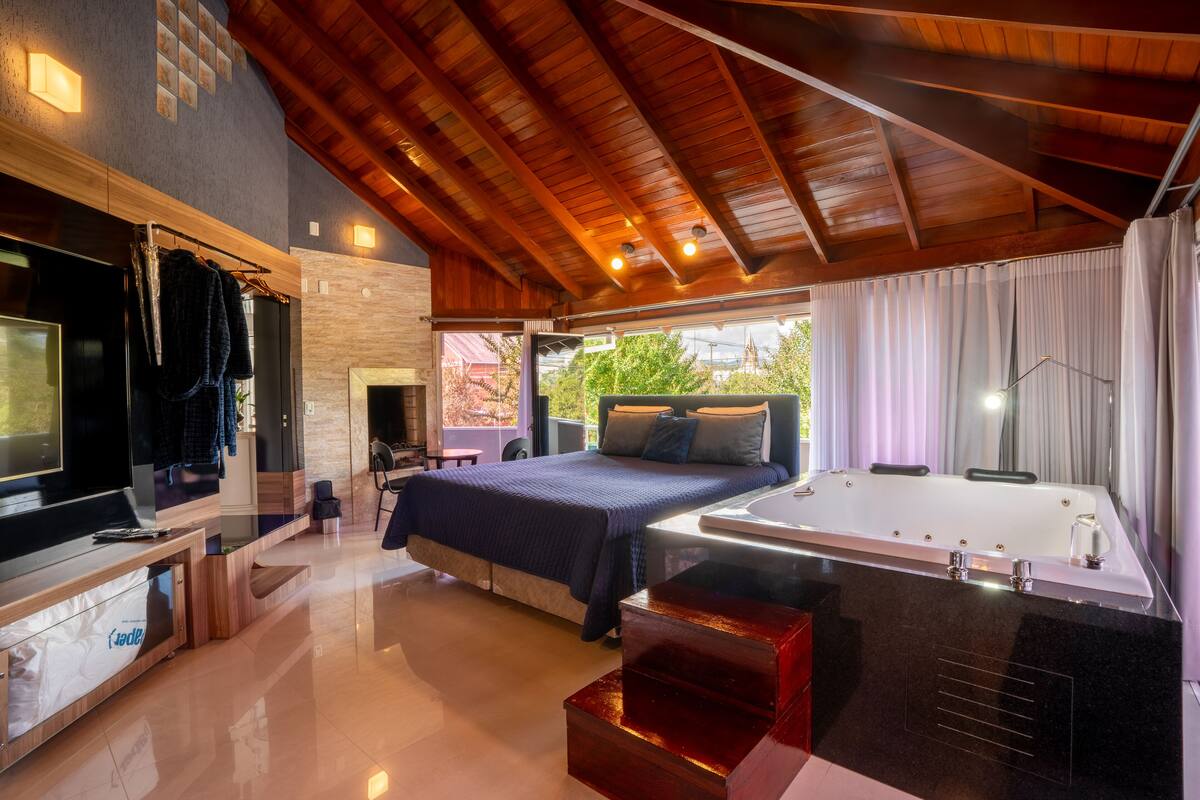 Un dormitorio moderno con una cama grande, televisión integrada, bañera y vistas al exterior.