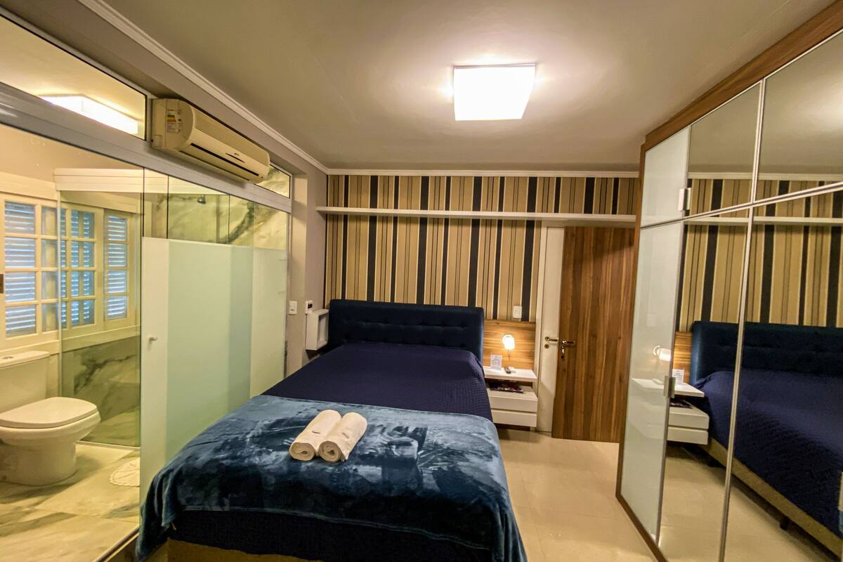 Una habitación de hotel moderna con una cama, una mesita de noche, un espejo y una zona de ducha.