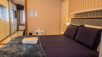 Quarto de hotel com cama, escrivaninha, cadeira, guarda-roupa e mesa de cabeceira.
