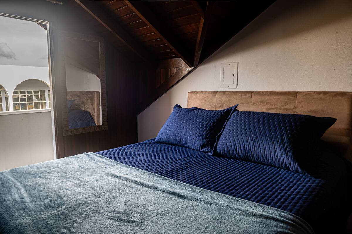 Un dormitorio con techo inclinado, cabecera de madera y un ventanal con vistas a un edificio.