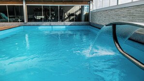 An indoor swimming pool with clear water, a glass wall, and a metal railing. - FIKA Residence (Dois Irmaos)