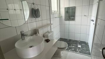 A modern bathroom with a large white sink, a toilet, and a shower area.