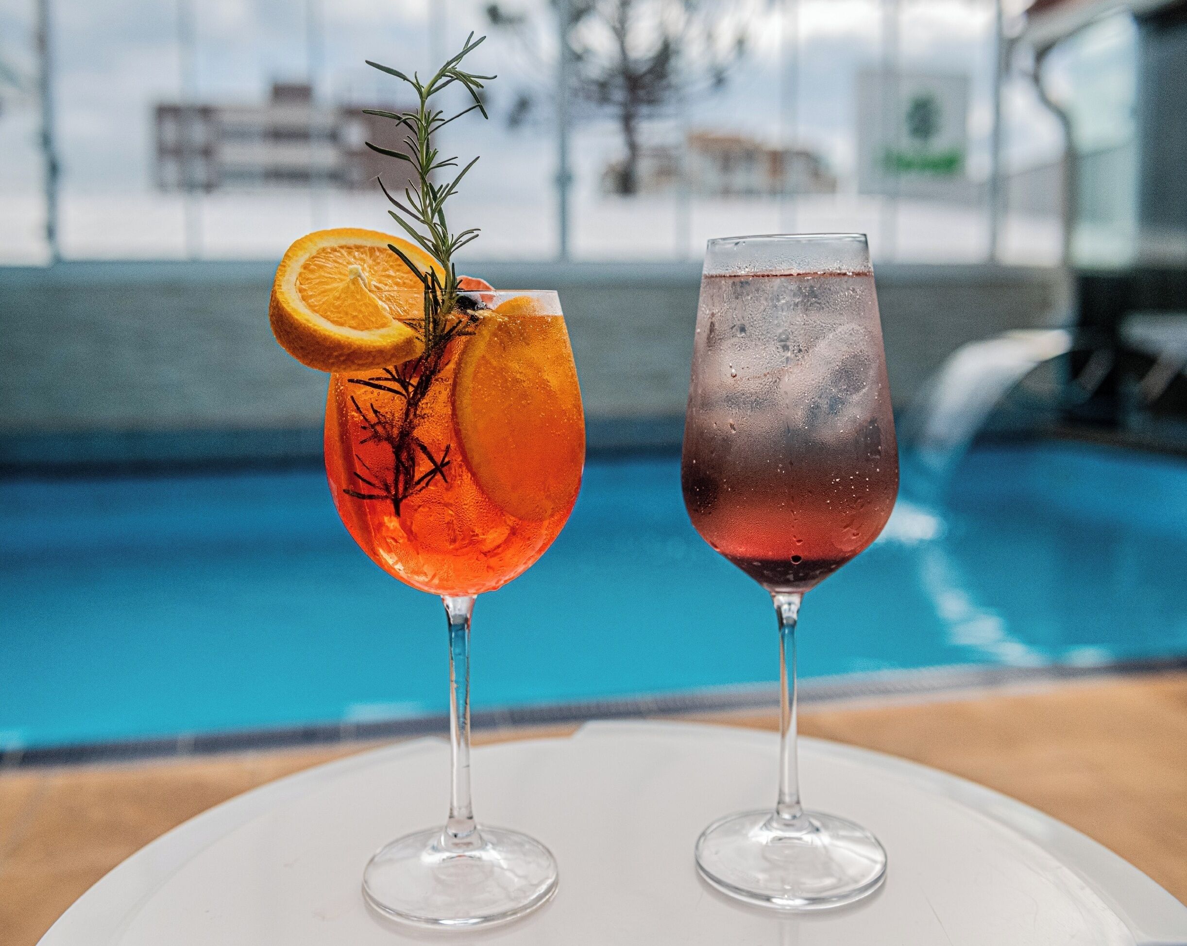 Dos vasos de cócteles con una piscina al fondo.