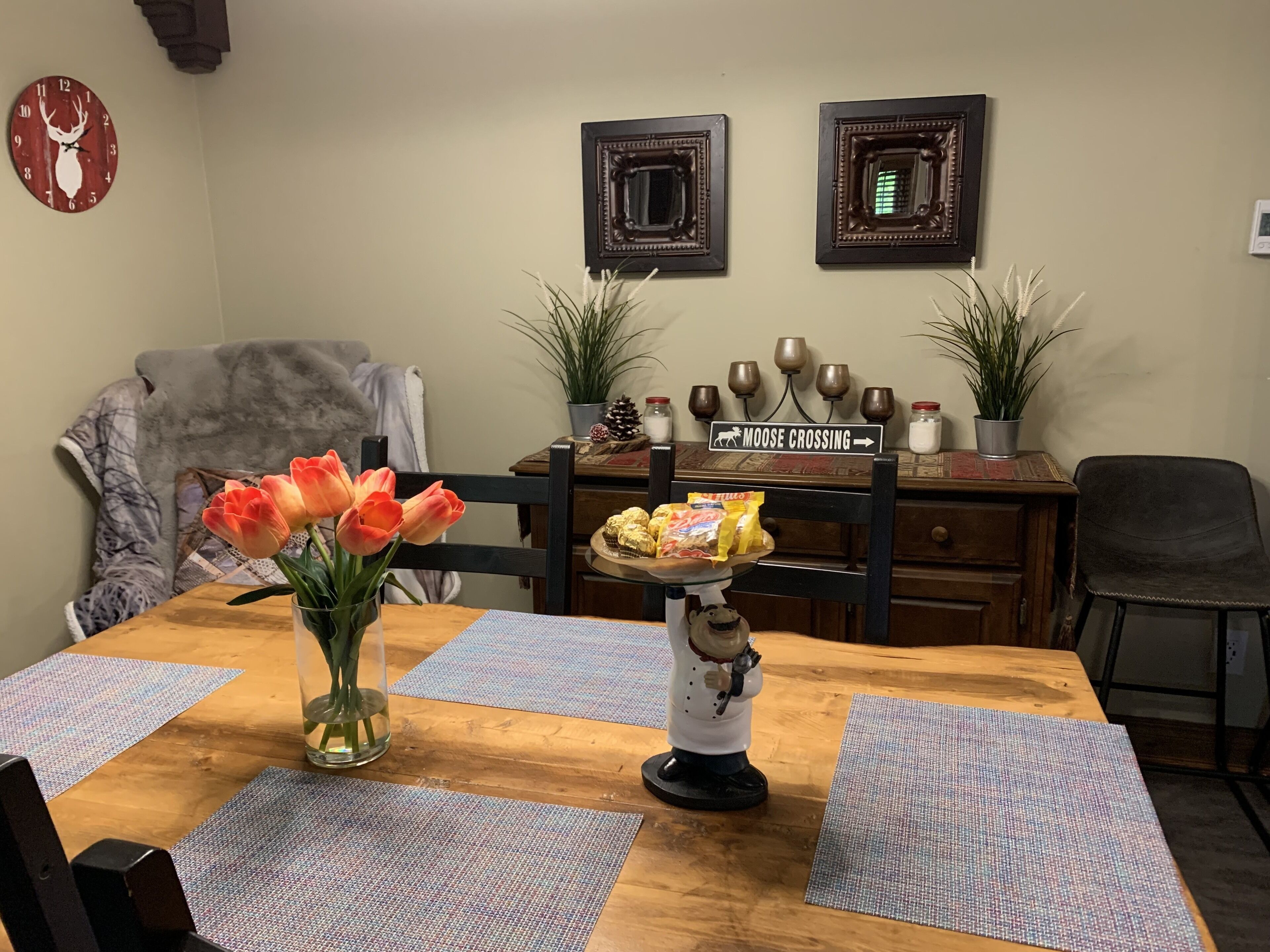A dining table with a vase of tulips, a decorative plate with snacks, and a moose crossing sign.