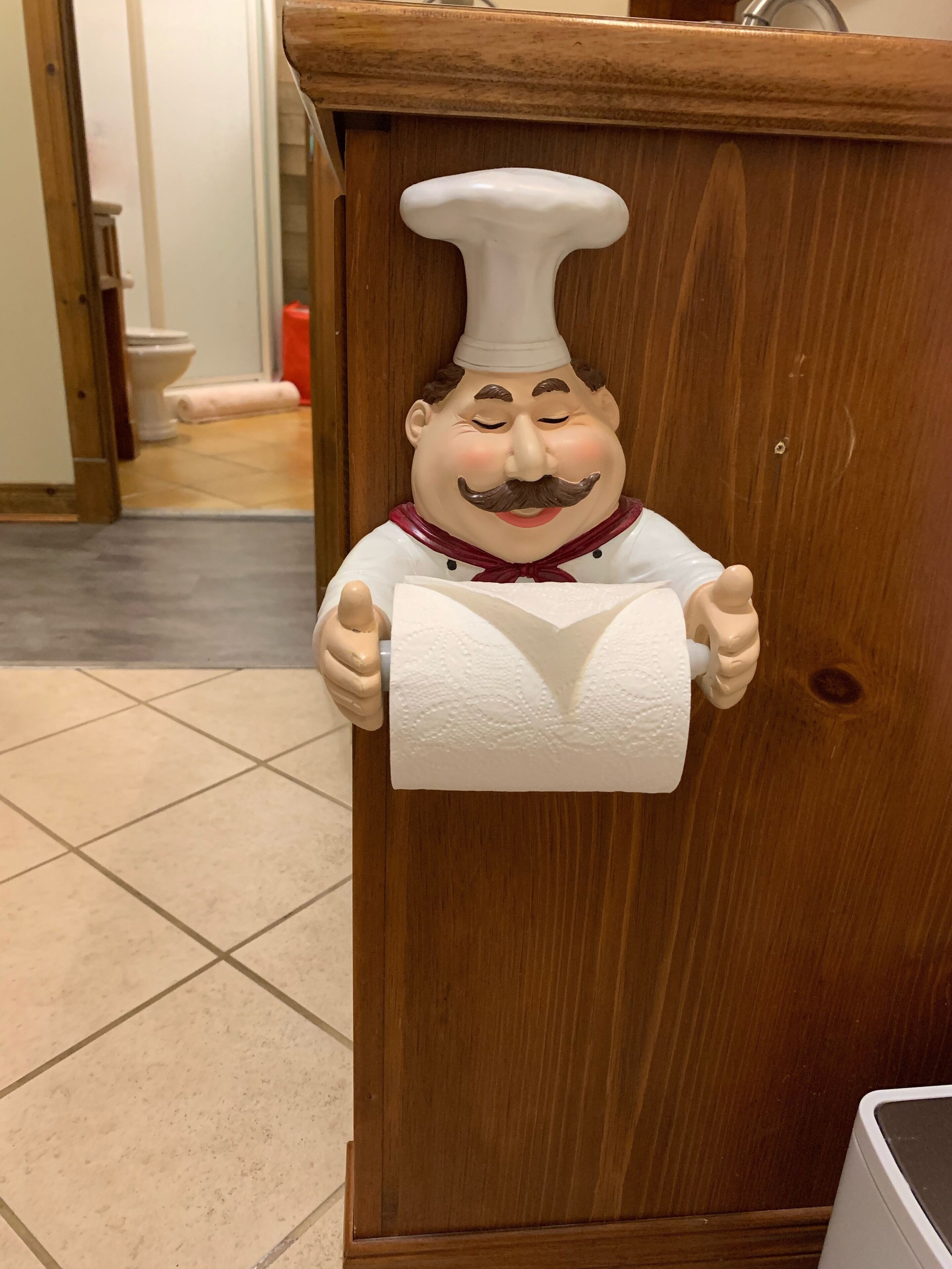 A wooden cabinet with a decorative figure holding a roll of toilet paper.
