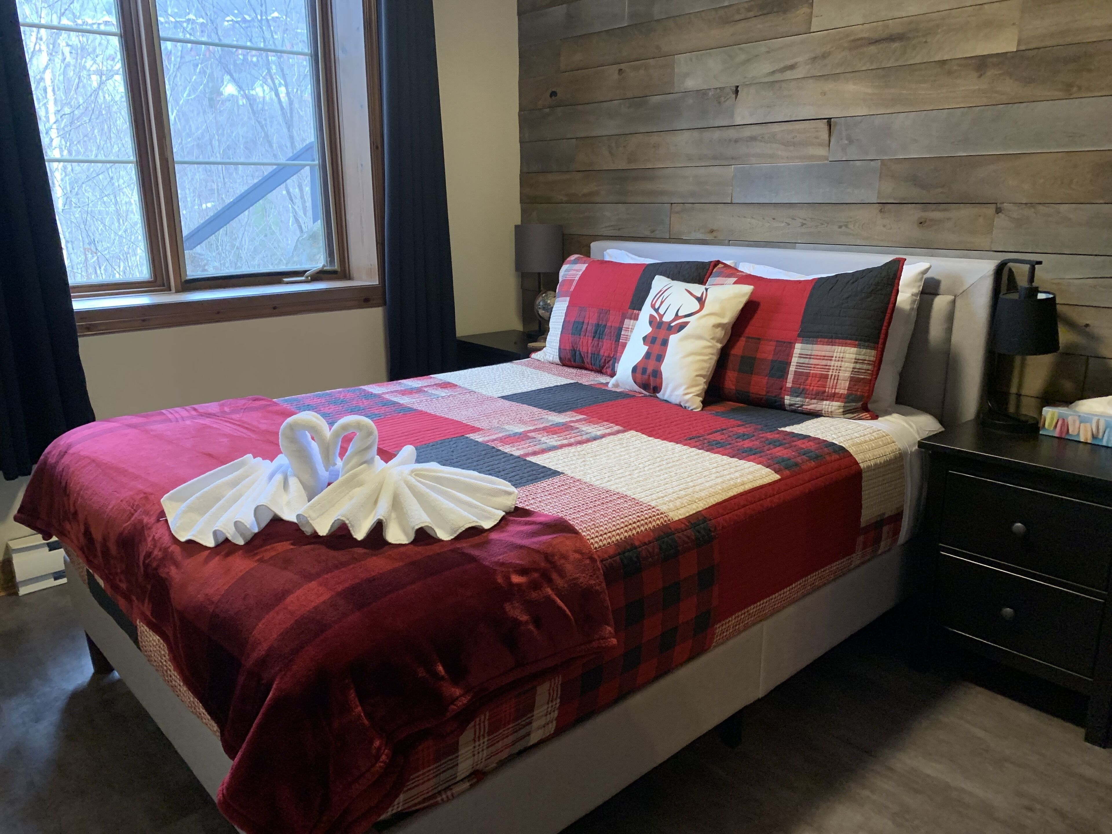 A neatly made bed with a red and white quilt, two pillows with a deer design, and a swan-shaped towel on the bed.