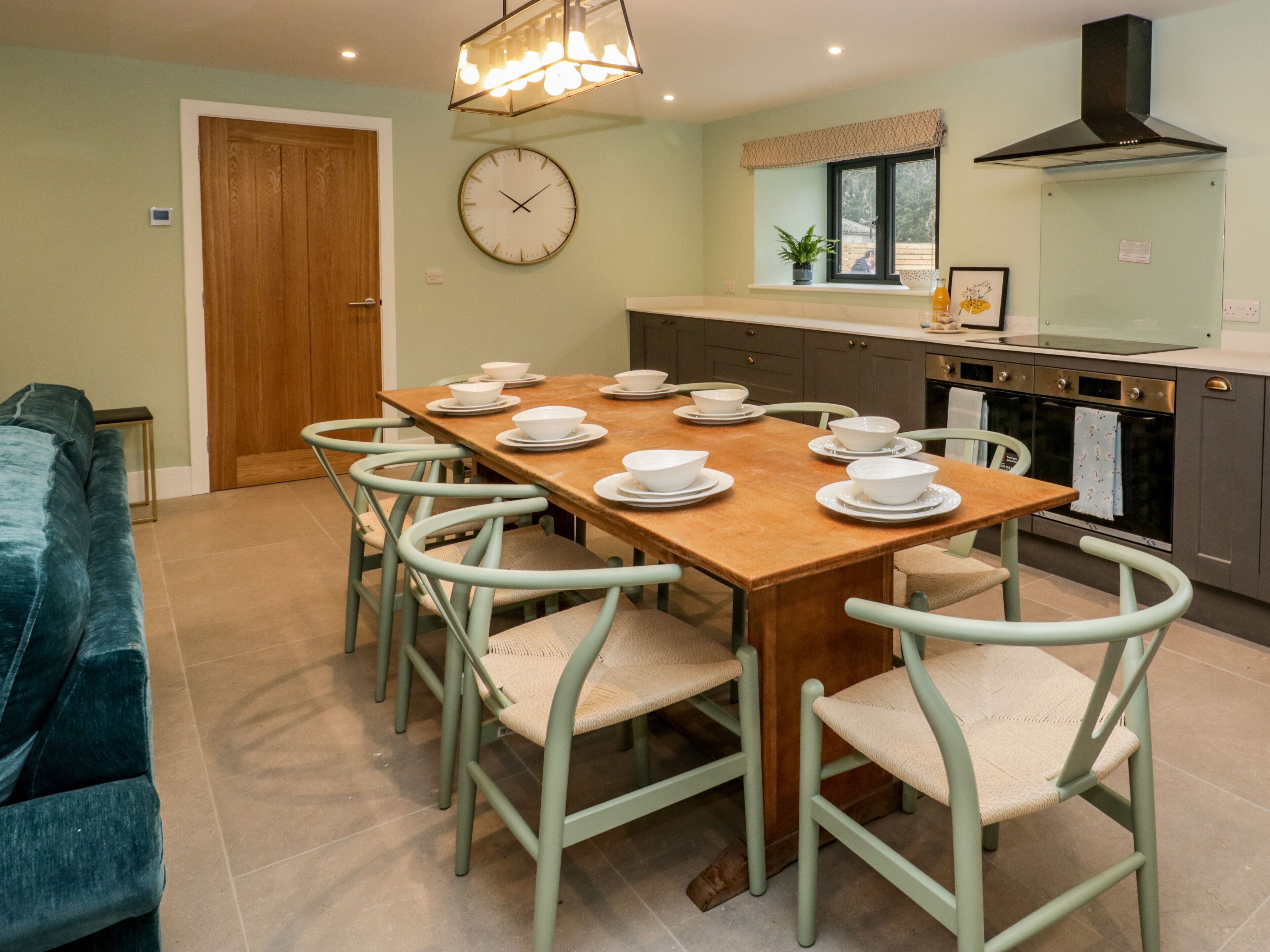 Un coin repas avec une table en bois dressée pour six personnes, entourée de six chaises à assise en osier tressé.
