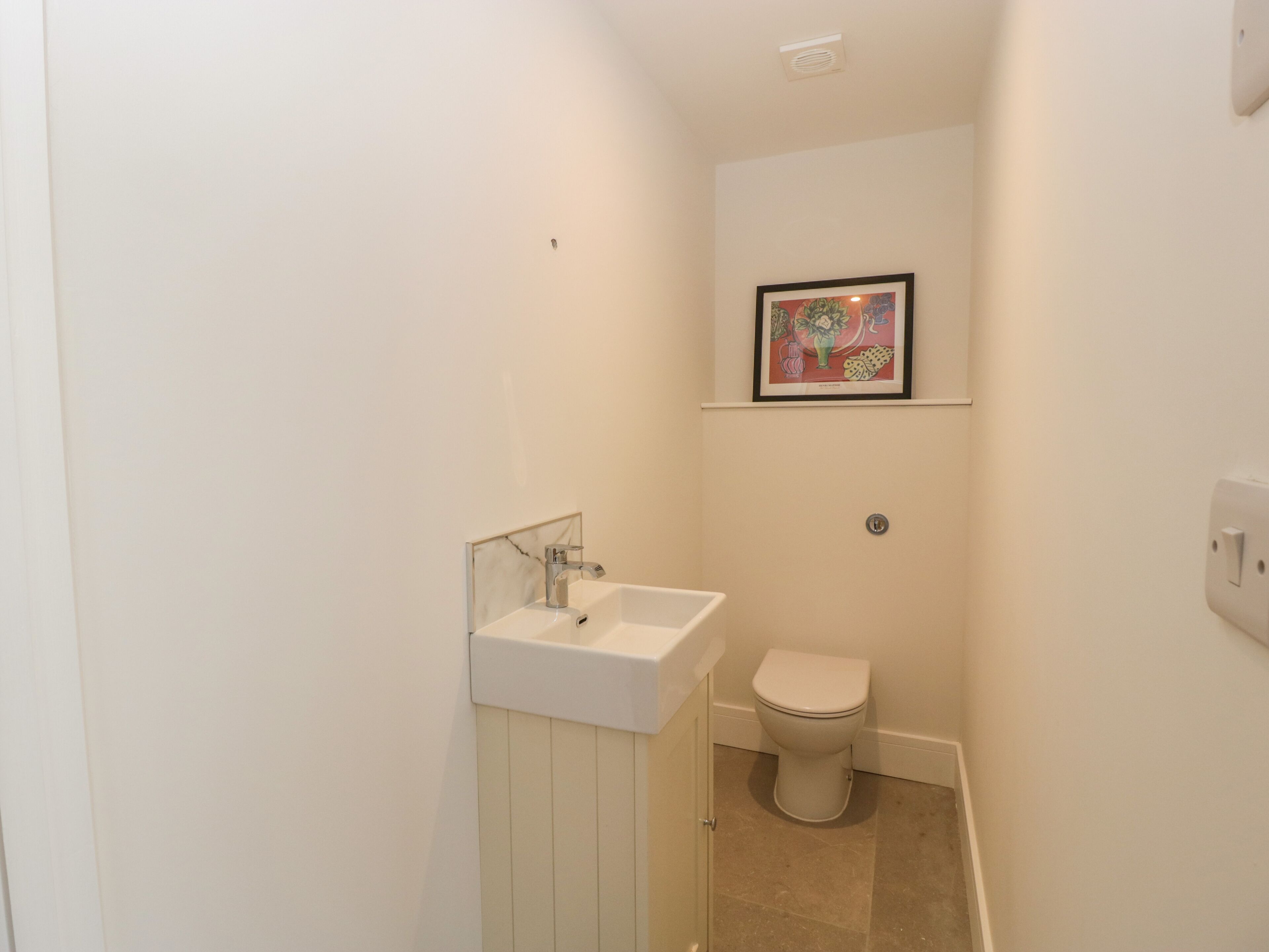 Un baño pequeño y blanco con un lavamanos blanco, un inodoro y un cuadro en la pared.