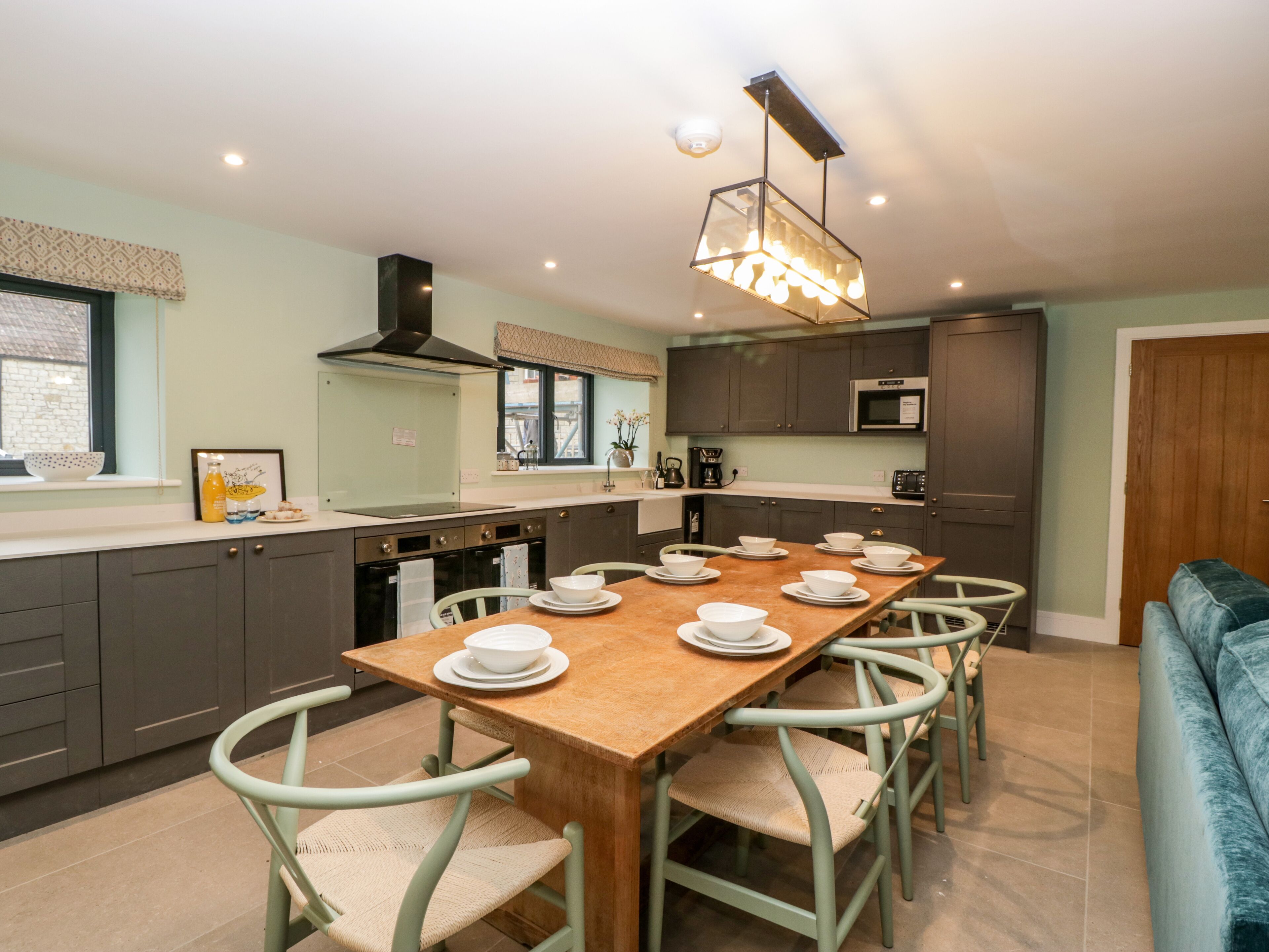 A modern kitchen with a long dining table, grey cabinets, and a hanging light fixture.