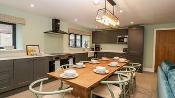 A modern kitchen with a long dining table, grey cabinets, and a hanging light fixture.