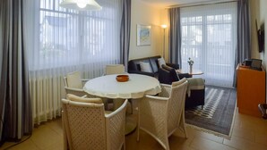 A well-lit living room with a round dining table, white chairs, a sofa, and a TV on a stand. - Apartment with 1 bedroom and balcony (Ostseebad Binz)