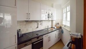 A modern kitchen with white cabinets, a black countertop, stainless steel appliances, and a window providing natural light. - Apartment with 1 bedroom and balcony (Ostseebad Binz)