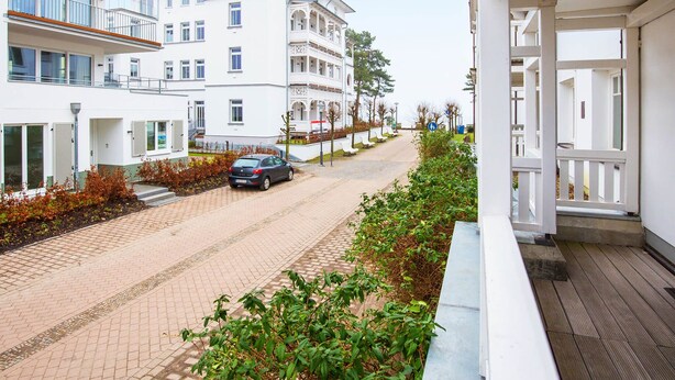 A multi-story building with balconies, a paved street, and a car parked on the side. - Apartment with 1 bedroom and balcony (Ostseebad Binz)