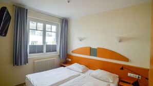 A hotel room with a double bed, a nightstand, a lamp, and a window with curtains. - Apartment with 1 bedroom and balcony (Ostseebad Binz)