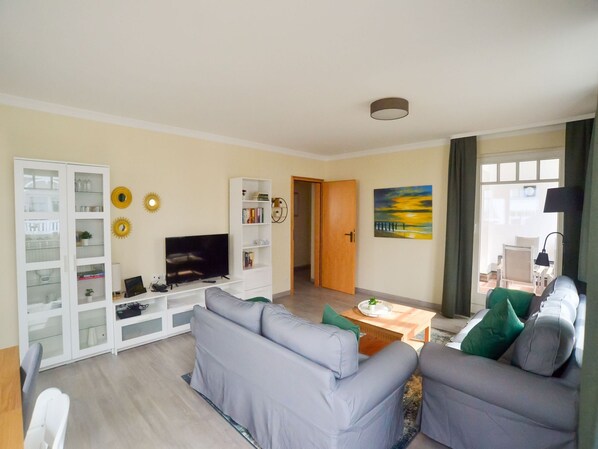 A living room with a grey sofa, a TV, a bookshelf, and a painting on the wall.