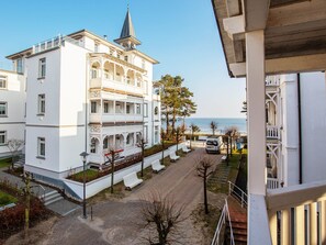 A multi-story white building with a prominent tower and balcony, situated by a coastal road with benches and a parked van. - Apartment with 1 bedroom and balcony (Ostseebad Binz)