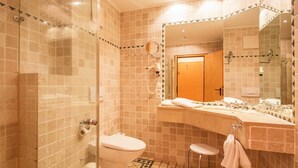 Un baño con ducha de vidrio, inodoro, lavabo con espejo y piso estampado.