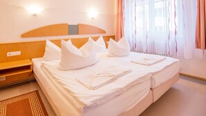 Una habitación de hotel con una cama grande, dos mesitas de noche, un cabecero de madera y una ventana con cortinas.
