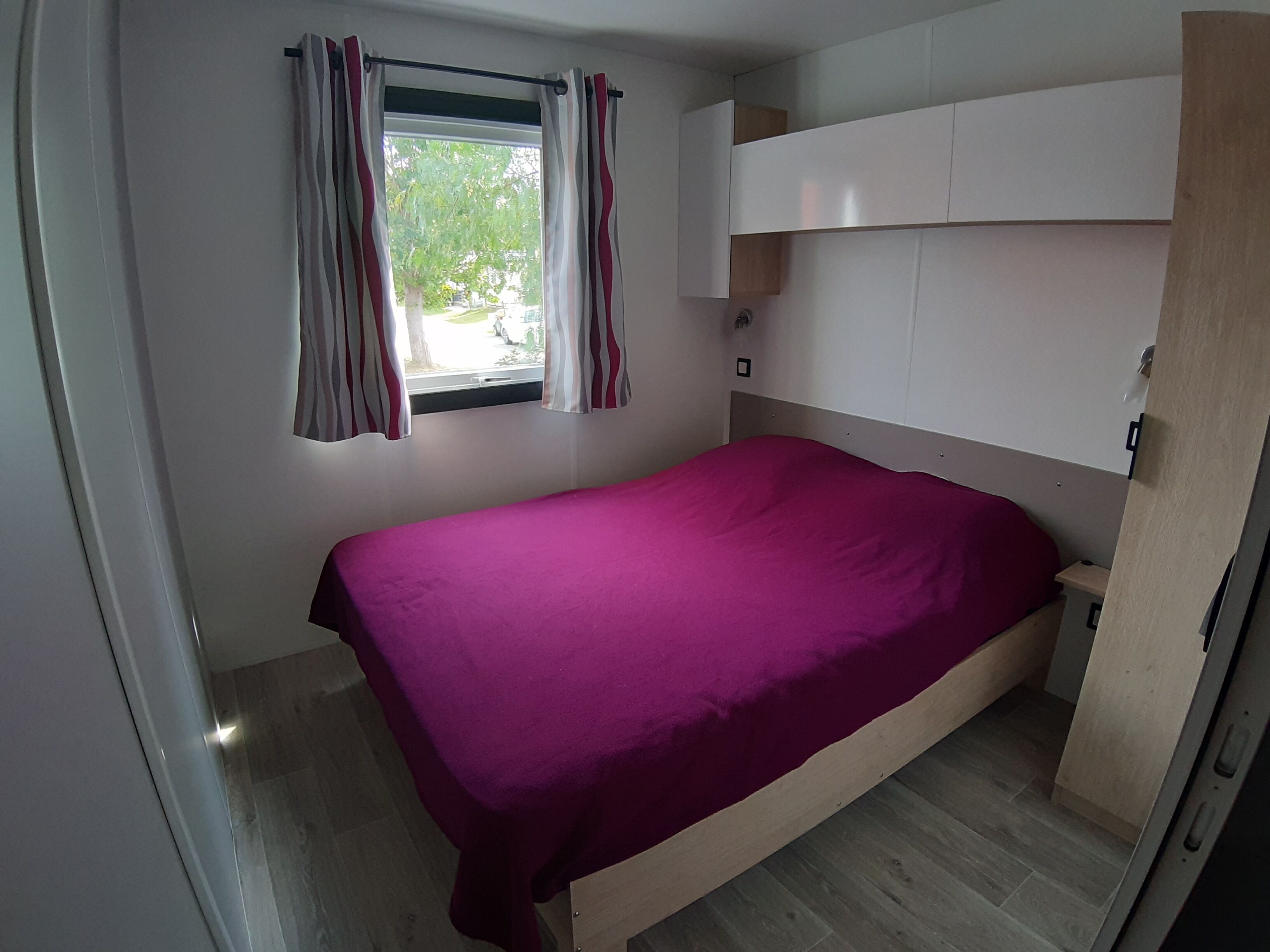 A bedroom with a bed, a window with curtains, a wardrobe, and a small bedside table.