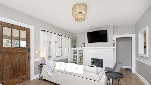Een woonkamer met een witte bank, een televisie boven een open haard en een houten deur.