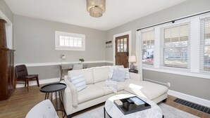 Een woonkamer met een beige modulaire bank, een ronde salontafel, en een eethoek met een kleine tafel en stoelen.