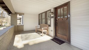 Een overdekte veranda met een bank, een houten deur en een welkomstmat.