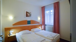Quarto de hotel com cama, mesas de cabeceira, luminária na parede, janela com cortinas e um quadro na parede.