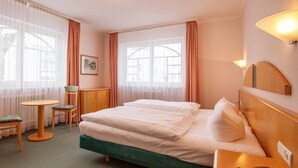 Ein Hotelzimmer mit einem Bett, einem Schreibtisch mit Telefon, einem Sessel, einem kleinen Tisch und einer Heizung.