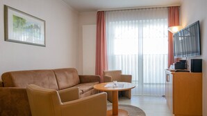 Une chambre d’hôtel moderne équipée d’un canapé, d’un fauteuil, d’une table ronde et d’un téléviseur posé sur un meuble.