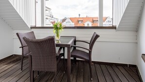 Ein Balkon mit Korbstühlen, einem Tisch und einem Blumenvasen, mit Blick auf Gebäude.