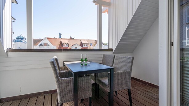 Un balcon avec une table et des chaises en osier, donnant sur un quartier résidentiel avec des maisons aux toits rouges.