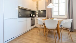 Une cuisine moderne avec des armoires blanches, un comptoir noir et un four encastré. On y trouve également un coin repas avec une table en bois et des chaises blanches.