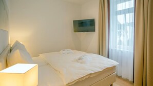Ett hotellrum med en säng, en sänglampa, en platt-TV och ett fönster med gardiner.