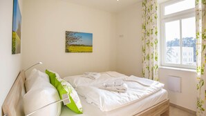 Ein Zimmer mit einem Einzelbett, einem Holzrahmen, weißer Bettwäsche, einem grünen Kopfkissen und einem Landschaftsbild an der Wand.