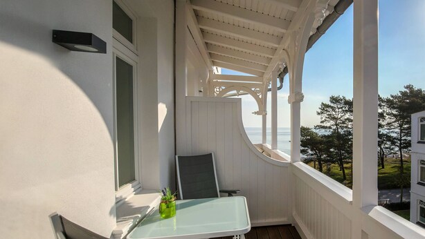 Ein Balkon mit Glastisch und Stühlen, einem Blumentopf und Blick auf das Meer.
