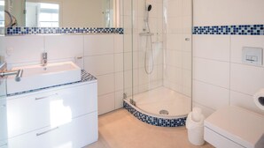 Ein modernes Badezimmer mit einer Duschkabine, einem weißen Waschbecken und einer Toilette.