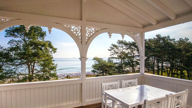 A covered outdoor seating area with a view of the sea and trees. - Apartment with sea view, 2 bedrooms and balcony (Ostseebad Binz)