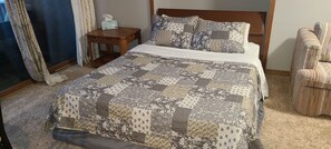 A bedroom with a bed, a nightstand, a chair, and a window with curtains.