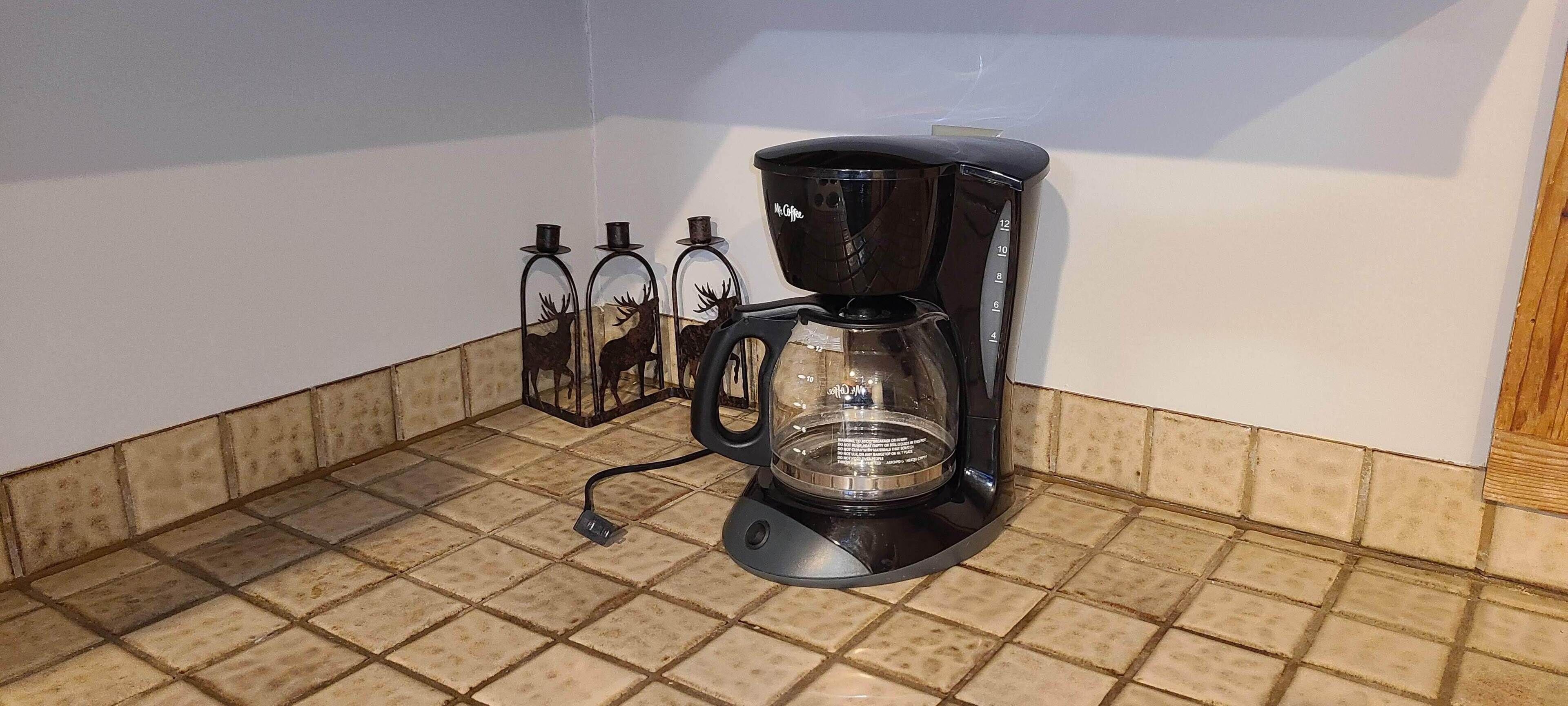 Een koffiezetapparaat op een betegeld aanrecht met een witte muur en houten lambrisering.