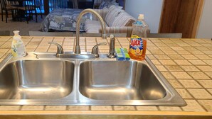 A kitchen with a double stainless steel sink, a faucet, and various cleaning supplies on the counter.