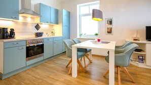 A modern kitchen with light blue cabinets, a white dining table, and a wooden floor. - Apartment with sea view, 1 bedroom and balcony (Ostseebad Binz)