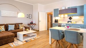 A modern living room with a brown sectional sofa, a white coffee table, and a dining area with two chairs and a table. - Apartment with sea view, 1 bedroom and balcony (Ostseebad Binz)