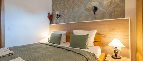A neatly made bed with a green quilt, a wooden headboard, and two bedside lamps.