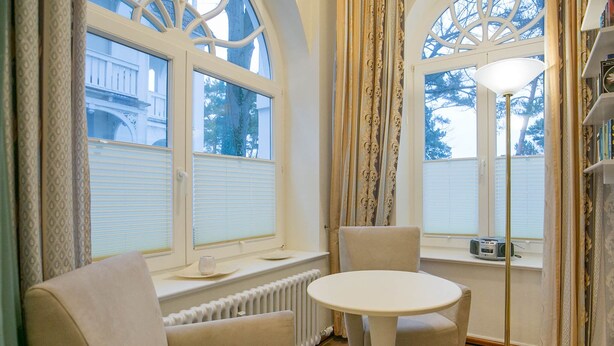 A room with a round table and two chairs, a radiator below the windows, and a floor lamp. - Apartment with sea view and 2 bedrooms (Ostseebad Binz)