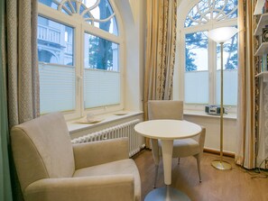 A room with a round table and two chairs, a radiator below the windows, and a floor lamp. - Apartment with sea view and 2 bedrooms (Ostseebad Binz)