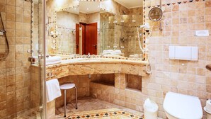 Une salle de bain avec un lavabo en marbre aux lignes courbes, une douche en verre, des toilettes et un petit tabouret.