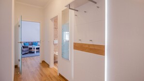 A hallway with a wooden floor, a glass door leading to a living area with a sofa and a coffee table, and a bathroom with a shower and toilet. - Apartment with sea view and 1 bedroom (Ostseebad Binz)