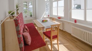 A bright room with a wooden floor, a red sofa, a wooden table, and a window with blinds. - Apartment with sea view and 1 bedroom (Ostseebad Binz)