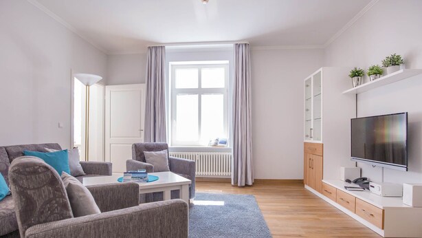 A modern living room with a sofa, armchairs, a coffee table, and a TV.